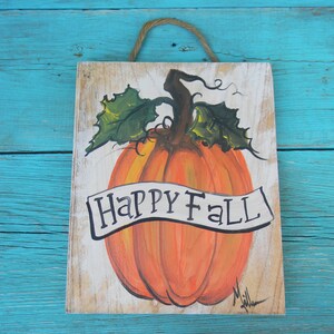 May include: A wooden sign with a painted orange pumpkin and green leaves. The sign says "Happy Fall" in black lettering.