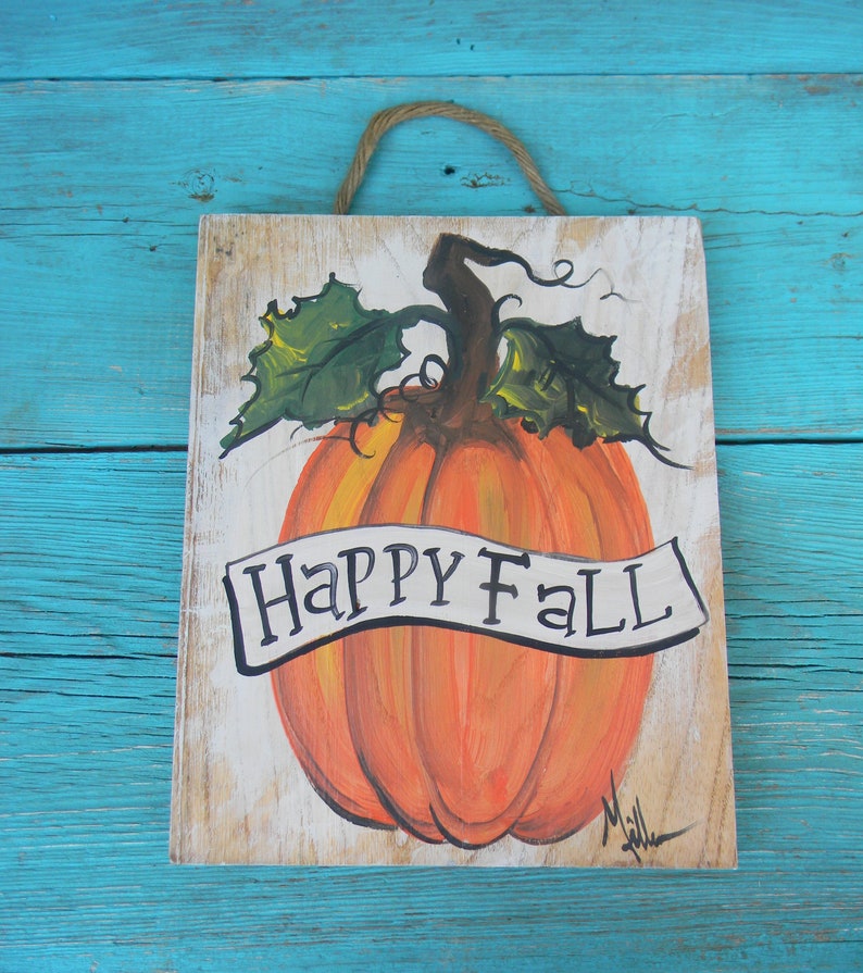 May include: A wooden sign with a painted orange pumpkin and green leaves. The sign says "Happy Fall" in black lettering.