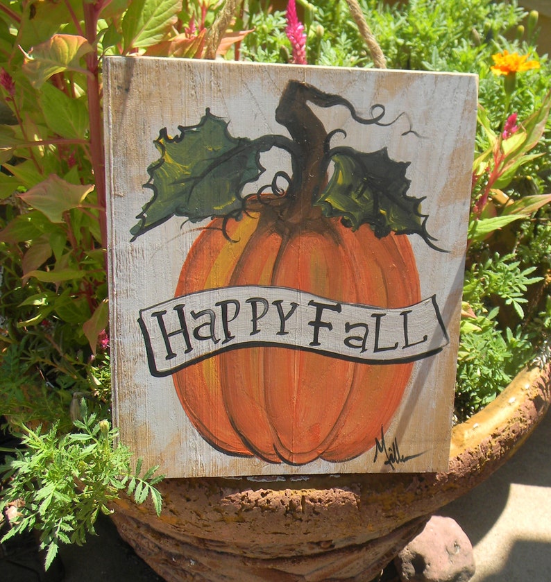 May include: A wooden sign with a painted orange pumpkin and green leaves. The sign says "Happy Fall" in a white banner.