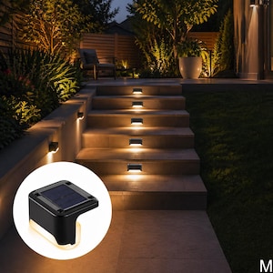 May include: Outdoor solar-powered step lights illuminate a stone staircase at dusk. The lights are rectangular and emit a warm glow. The scene includes lush greenery and a seating area, creating a welcoming ambiance for a garden or patio.
