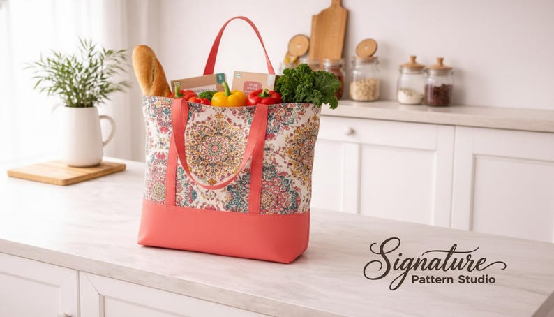 May include: A coral and patterned tote bag filled with groceries, including a baguette, vegetables, and packaged goods. The bag has coral handles and a coral bottom. The bag is sitting on a white countertop.