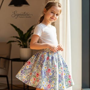 May include: A young person wearing a white t-shirt and a floral print skirt. The skirt features a pattern of pink, purple, and yellow flowers on a light blue background. The text "Signature Pattern Studio" is visible in the background.