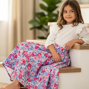 May include: A young person wearing a white top with ruffled sleeves and a long floral skirt, sitting on wooden stairs. The skirt features a pattern of pink and blue flowers. The image includes the text "Signature Pattern Studio".
