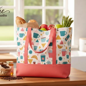 May include: A patterned tote bag filled with groceries, including bread, apples, and asparagus. The bag has a design of coffee cups, croissants, and geometric shapes. The base of the bag is coral, and the handles are pink. The text "Signature Pattern Studio" is visible.