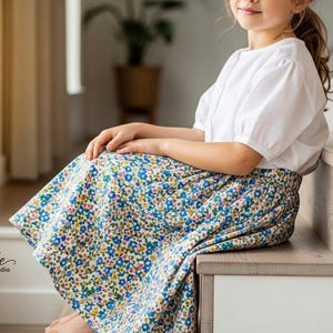 May include: A white blouse with puffed sleeves and a floral print skirt. The skirt features a blue background with yellow, blue, and pink flowers. The "Signature Pattern Studio" logo is visible in the lower left corner.