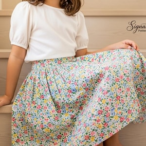 May include: A white short-sleeved top paired with a floral print skirt. The skirt features a pattern of small flowers in shades of pink, blue, and yellow on a light background. The image includes the text "Signature Pattern Studio".