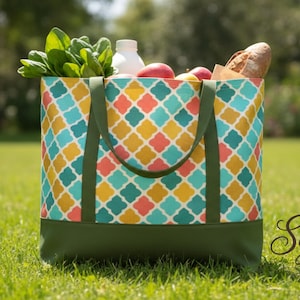 May include: A patterned tote bag filled with groceries, including fresh produce and a loaf of bread. The bag has a geometric design in teal, yellow, and coral, with green handles and a green base. The bag is on a grassy lawn.