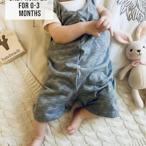 May include: A baby wearing a gray striped romper with a white shirt underneath, lying on a cream-colored cable knit blanket. A stuffed bunny with a pink bow and a wooden block with the word "handmade" are also in the image. Text on the image reads "CUSTOMIZABLE BABY ROMPER FOR 0-3 MONTHS."