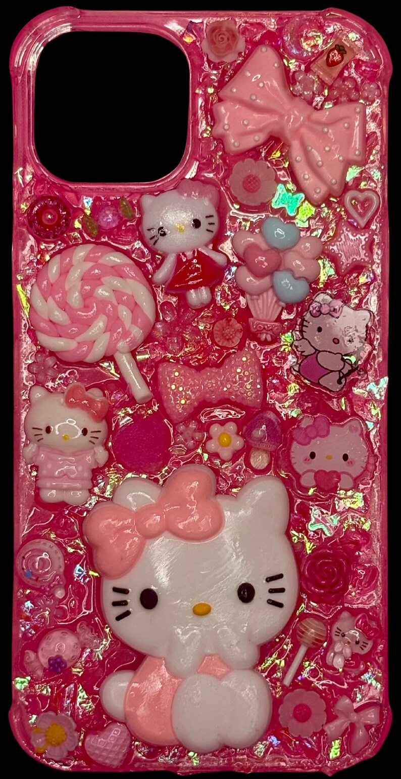 Puede incluir: Funda de tel&eacute;fono rosa decorada con varios adornos 3D. Presenta m&uacute;ltiples figuras de Hello Kitty, lazos, corazones, flores y una piruleta. La funda est&aacute; llena de purpurina rosa y otros elementos decorativos.