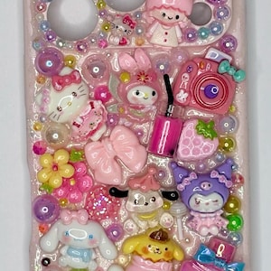 Puede incluir: Funda de tel&eacute;fono rosa decorada con varios abalorios 3D, incluyendo Hello Kitty, My Melody y otros personajes de dibujos animados. La funda est&aacute; adornada con cuentas, lazos y un frasco de perfume, creando un dise&ntilde;o lindo y colorido.