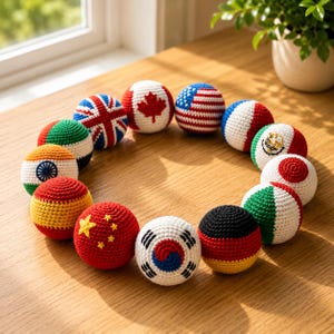 May include: A circular arrangement of crocheted balls, each displaying a different national flag. Flags include the UK, Canada, USA, France, Mexico, Japan, Italy, India, Spain, China, South Korea, and Germany. The balls are displayed on a wooden surface, with a plant in the background.
