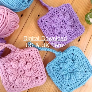May include: Crocheted square coasters in shades of purple, pink, and blue, with a floral design. The coasters have a small loop for hanging. The image also shows balls of yarn in matching colors. The text "Digital Download US & UK Term" is visible.