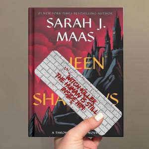 May include: A rectangular bookmark with a white brick pattern and red text that reads: WITCH KILLER THE HUMAN IS STILL INSIDE HIM. The bookmark is positioned over a book titled Queen of Shadows by Sarah J. Maas with a dark red and black cover.