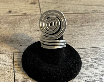 Könnte beinhalten: Ein silberner Ring mit einem Spiraldesign. Der Ring befindet sich auf einem schwarzen Samtringhalter.