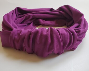 May include: A purple fabric headband with a knotted design. The headband is made of a soft, stretchy material.