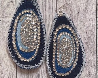 May include: A pair of denim earrings with a swirl design and rhinestones. The earrings are blue and silver.