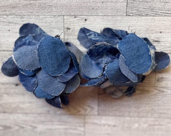 May include: Two denim flower arrangements made of blue jean fabric scraps. The flowers are arranged in a circular shape and are made of various sizes of denim circles.