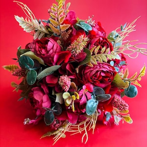 May include: A bouquet of deep red and burgundy flowers, including peonies and other blooms, with green and yellow accents. The arrangement is set against a bright red background, creating a striking contrast.