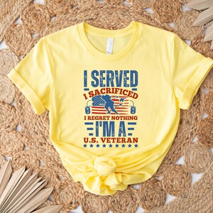 May include: A yellow t-shirt with the text "I SERVED I SACRIFICED I REGRET NOTHING I'M A U.S. VETERAN" in blue and red. The design includes an American flag and a silhouette of a soldier. The shirt is folded.