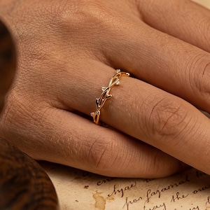 May include: A gold ring featuring a detailed branch design, embellished with tiny, glittering elements. The ring is displayed on a finger, highlighting its intricate craftsmanship. The ring's design evokes nature, with an emphasis on organic forms and textures.