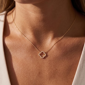 May include: A gold-toned chain necklace featuring a central four-leaf clover pendant. The clover charm is outlined with small, clear, sparkling stones set along its entire perimeter, creating a delicate and refined piece of jewellery.