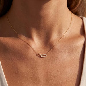 May include: A gold-toned chain necklace featuring a small, rectangular pendant link encrusted with tiny, clear, sparkling stones. The delicate chain connects to the central link, which has a slightly offset, interlocking design, creating a refined look.