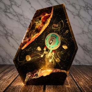 May include: A hexagonal resin display piece featuring a miniature starship model suspended in a dark, starry space scene. The scene includes a large, textured orange-brown asteroid at the top, smaller floating rocks, and a glowing base.