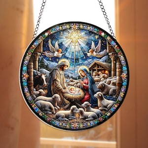 May include: Round stained glass window depicting the Nativity scene. The artwork features Mary, Joseph, baby Jesus, angels, sheep, and a bright star. The window is framed with a black border and a decorative floral pattern.