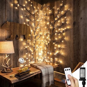 Könnte beinhalten: Eine Wand-Lichterkette in Form von dunklen, verzweigten Zweigen mit warmweißen LED-Lichtern. Die Lichter sind in einem vertikalen, baumartigen Muster an einer Holzwand angeordnet. Eine Fernbedienung ist im Vordergrund zu sehen.