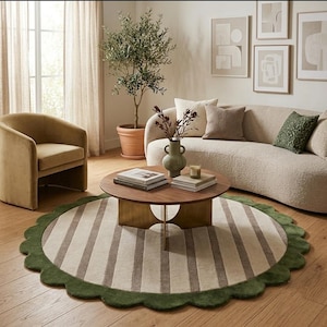 May include: A round area rug featuring a striped pattern in shades of beige and brown, finished with a scalloped dark green border. The rug is positioned on a wooden floor, serving as a central element in a room with a sofa, armchair, and table.