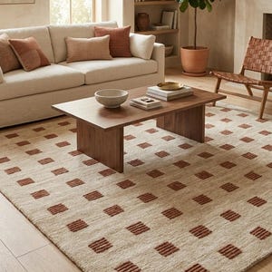 Puede incluir: Alfombra beige con un patrón repetido de cuadrados color óxido. La alfombra está colocada en un salón con una mesa de centro de madera, un sofá beige y una silla de cuero trenzado. La habitación tiene una paleta de colores neutros.