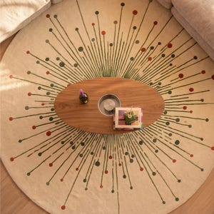 May include: A large round area rug in cream featuring a radiating starburst pattern of thin green lines tipped with small red and dark green circles. The design extends outward from the center, creating a symmetrical, sunburst-like visual effect.