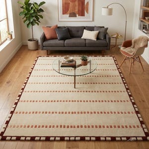 Puede incluir: Una alfombra rectangular con base de color crema y filas horizontales de peque&ntilde;os mechones rectangulares de color terracota. La alfombra est&aacute; enmarcada por un borde s&oacute;lido de color marr&oacute;n oscuro con un patr&oacute;n de cuadrados color crema.