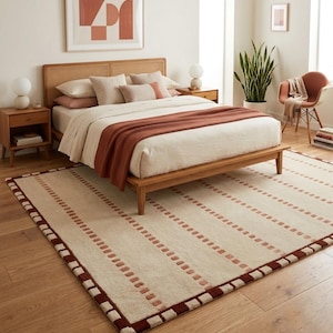Puede incluir: Una alfombra rectangular con una base de color crema y rayas verticales repetitivas compuestas por peque&ntilde;os patrones cuadrados de color rojo oscuro. La alfombra tiene un borde grueso de color rojo oscuro que enmarca el per&iacute;metro.