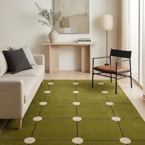Puede incluir: Una alfombra rectangular que presenta un fondo verde oliva sólido con una cuadrícula de líneas negras finas. En cada intersección de las líneas de la cuadrícula hay un pequeño parche circular de color blanco roto, creando un patrón.