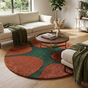 May include: A round area rug featuring a bold geometric pattern of large, interlocking burnt orange circles against a deep forest green background. The rug has a thick, textured pile and is positioned on a light-colored wooden floor in a living room.