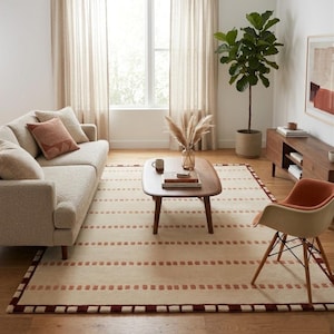 Puede incluir: Una alfombra rectangular con base de color crema, filas horizontales de peque&ntilde;os bloques rectangulares de color &oacute;xido y un borde marr&oacute;n oscuro. La alfombra est&aacute; colocada sobre un suelo de madera bajo una mesa de centro y un sof&aacute;.