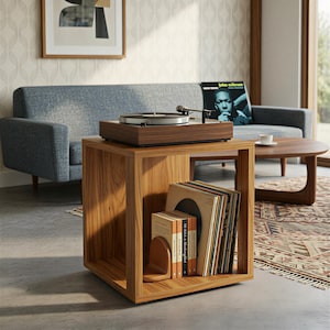 Op de afbeelding: Een houten platenspeler staat op een bijpassende kubusvormige tafel. De tafel bevat vinylplaten en een boekensteun. Een blauwe bank en een salontafel staan op de achtergrond. Een ingelijste foto hangt aan de muur.