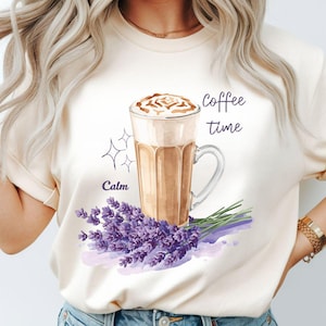 May include: Cream-colored t-shirt featuring a watercolor illustration of a coffee drink in a clear glass with a handle, a bouquet of purple lavender, and the words "Coffee time" and "Calm".