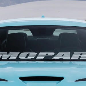 May include: A light blue car with the word "MOPAR" in white, stylized text across the windshield. The car is parked in front of a desert landscape.