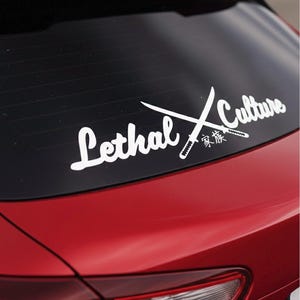 May include: White vinyl decal on a red car window. The decal features the words "Lethal Culture" in a cursive font, with two crossed swords and Japanese characters.