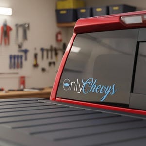 May include: Red truck bed with a black cover. The rear window features the text "Only Chevys" in a stylized font, with the Chevrolet logo. The background shows a garage setting with tools.