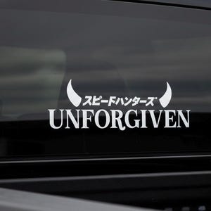May include: White vinyl decal with the text "UNFORGIVEN" below Japanese characters and a curved horn design. The decal is displayed on a black surface, likely a vehicle window.