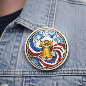 Könnte beinhalten: Ein runder Button mit einem Buntglasdesign der Liberty Bell mit roten, weißen und blauen Streifen und Tauben. Der Button ist weiß mit einem goldenen Rand und ist an einer Jeansjacke befestigt.