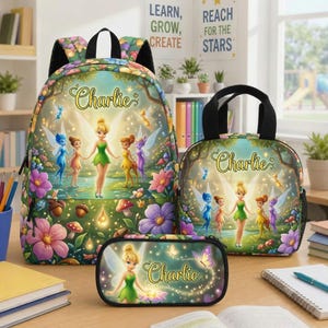 May include: A backpack, lunch bag, and pencil case set featuring Tinker Bell and fairy friends in a forest with flowers and mushrooms. Each item displays the name Charlie in gold script. The design includes colorful blossoms and glowing lights.