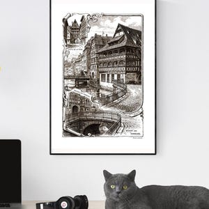 May include: Black and white framed print of a detailed architectural illustration of a European town with bridges, buildings, and the text "MAISON DES TANNEURS". The print is displayed on a white wall.