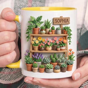 May include: A white ceramic mug with a yellow interior and handle, featuring a 3D-style graphic of a wooden shelf filled with various potted succulents, cacti, and colorful flowers. A small wooden sign on the top shelf displays the name SOPHIA.