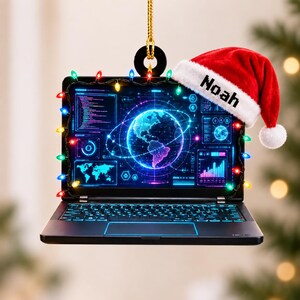 May include: A hanging ornament shaped like a laptop with a black frame, displaying a digital globe and data graphics on the screen. A string of colorful Christmas lights surrounds the screen, and a red Santa hat with the name Noah is attached.