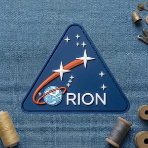 May include: A navy blue triangular patch featuring a stylized design of a planet with an orange orbit and white stars. The word "RION" is printed in white. The patch is likely an emblem or a decorative element.