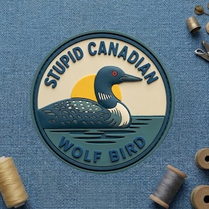 May include: A round, blue and white sticker with the text "STUPID CANADIAN WOLF BIRD" encircling a cartoon loon on water with a yellow sun in the background. The loon is blue with white accents and a red eye.